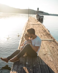 A man and his daughter sitting on a wooden plank near lake in Bedford, NH