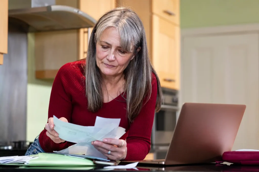 A lady reviewing household bills and financial documents while working in Bedford, NH